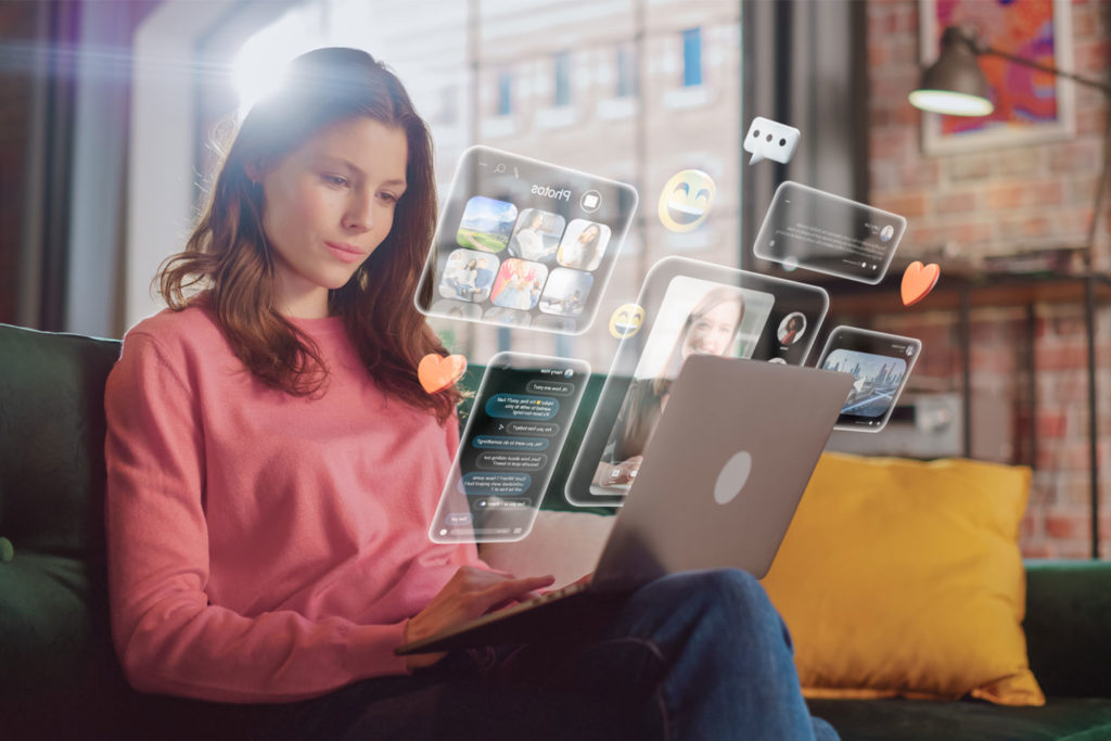 Junge Frau sitzt auf dem Sofa und durchstöbert Social Media auf einem Laptop.